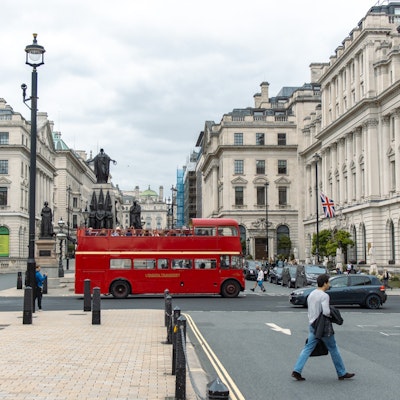 Photo of a red tour bus crossing Pall Mall, a wide street.