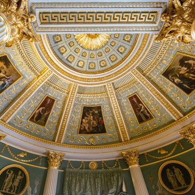 Photo of an intricately plastered ceiling, with paintings.