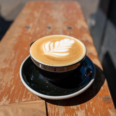 Photo of a flat white in a black cup on a bench.