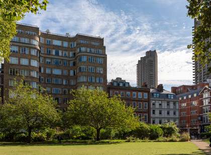 Photo of a grassy square, with a block of flats behind it.