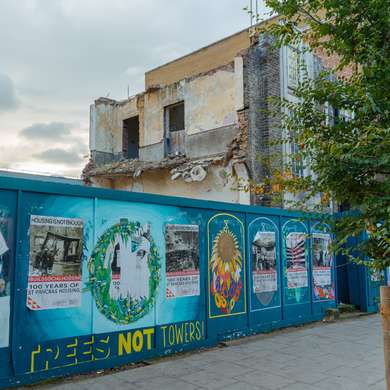 Photo of a partially demolished building hidden behind boards plastered with posters.