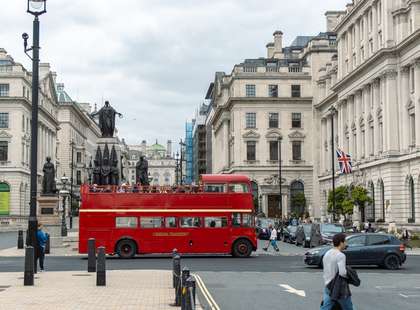 Photo of a red tour bus crossing Pall Mall, a wide street.