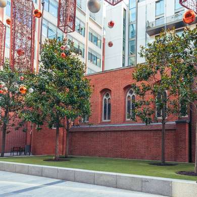 Photo of the exterior of the chapel,  a red brick church surrounded by glass & steel buildings.  Christmas decorations are in the foreground.

