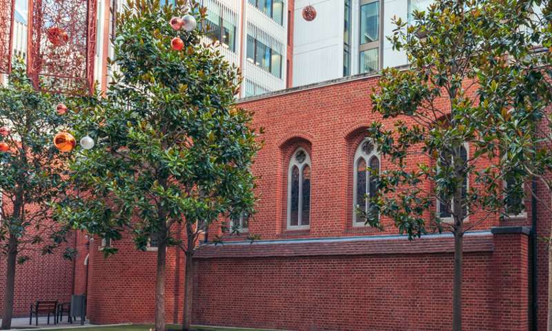 Photo of the exterior of the chapel,  a red brick church surrounded by glass & steel buildings.  Christmas decorations are in the foreground.
