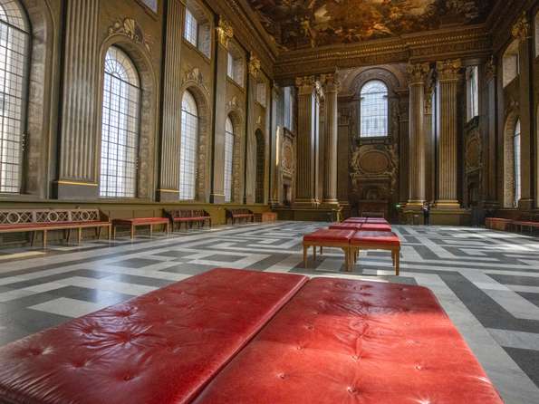 An enormous hall with dark green walls that are covered in paintings. There are red upolstered benches in the foreground.