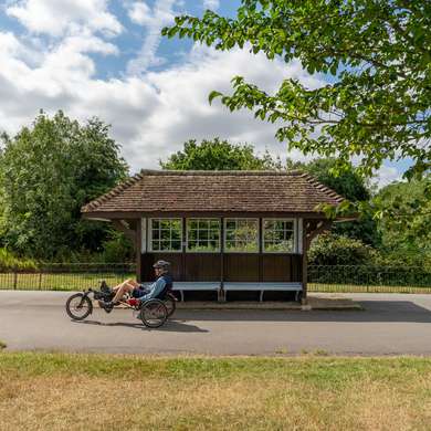 A picture of a man on a recumbant bicycle in front of a wooden shelter