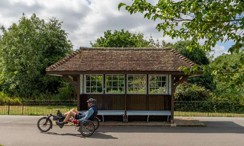 A picture of a man on a recumbant bicycle in front of a wooden shelter