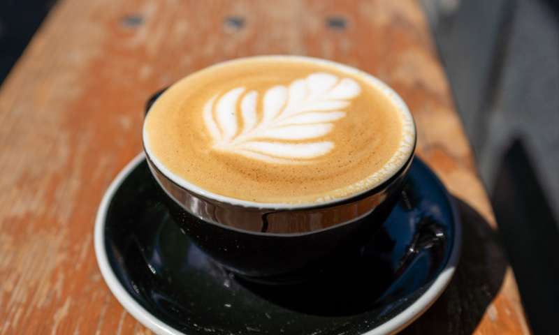 Photo of a flat white in a black cup on a bench.